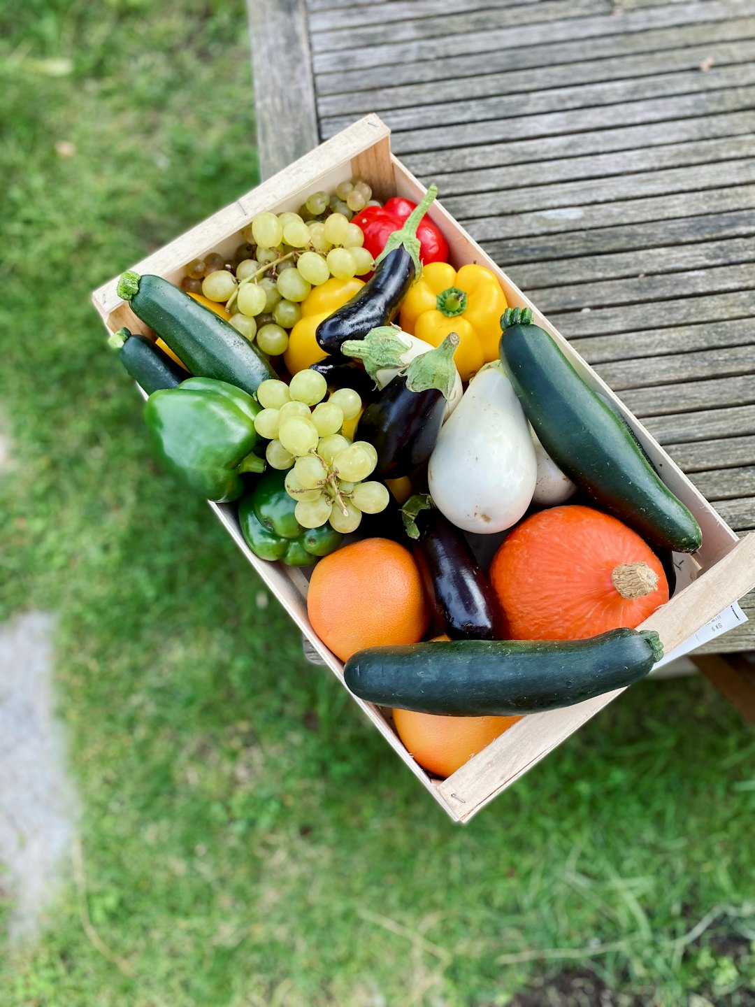 Caja de madera rebosante de frutas y verduras coloridas sobre una mesa de picnic.