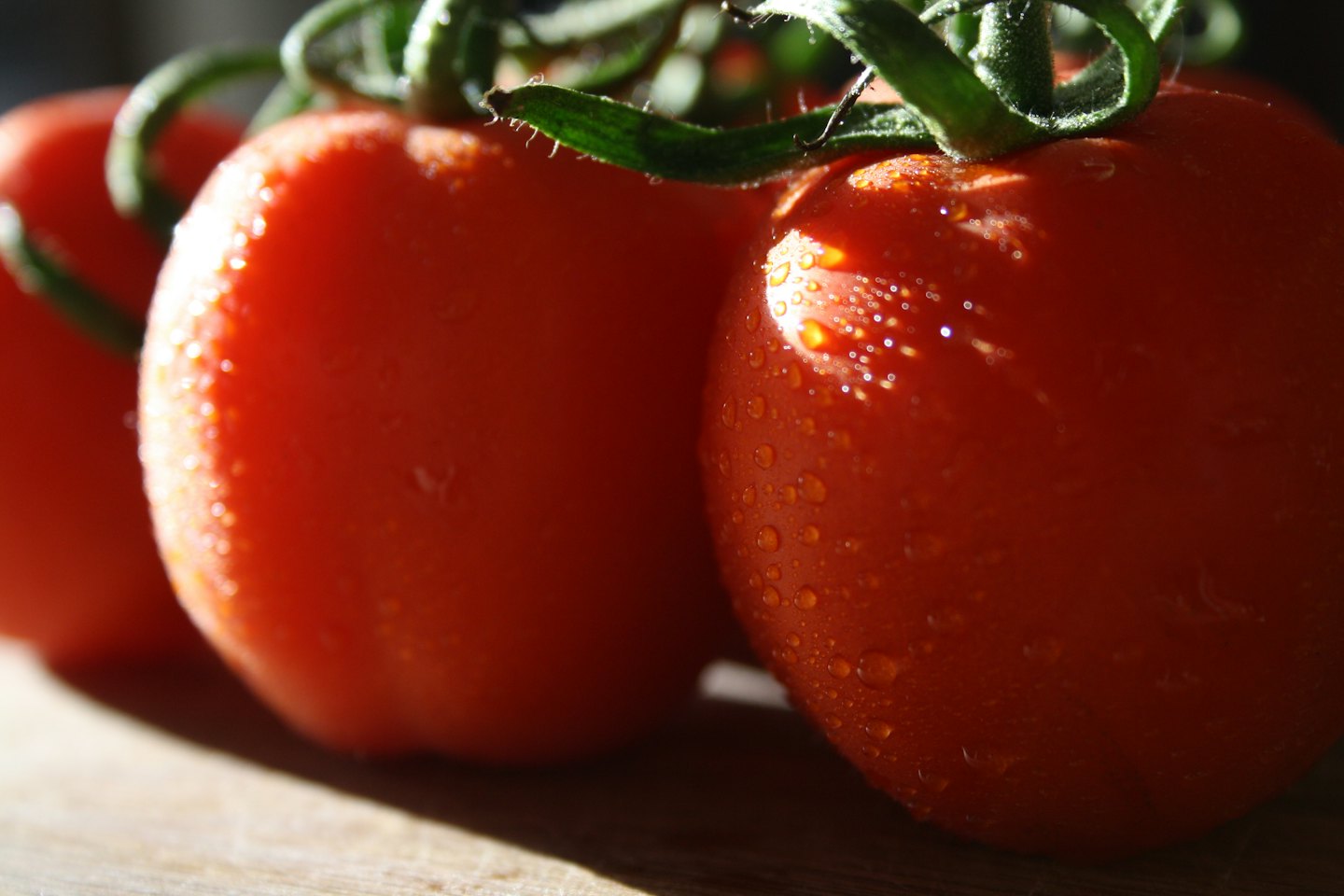 Tomates rojos frescos con gotas de agua sobre una superficie de madera.